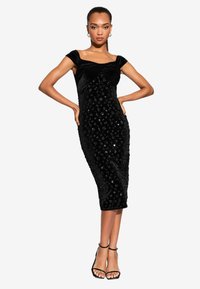 Melnas samta midi kleita ar bezplecu dizainu, rotāta ar spīdumiem, pieguļoša silueta un sānu šķēlums, kombinēta ar melniem sandaliem ar siksniņām.