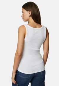 White ribbed tank top with a rounded neckline, fitted design, and wide shoulder straps, paired with dark denim pants.