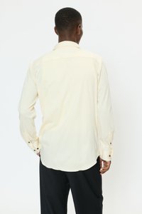 Lichtgele blouse met lange mouwen, een spreidkraag, knoopmanchetten en een rechte zoom. De stof lijkt glad met een subtiele textuur.