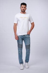 Fehér, rövid ujjú póló "Palm Spring" felirattal sárga színben, világoskék farmernadrággal, amely vízszintes bordázott részletekkel rendelkezik, és fehér sportcipővel.
