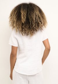 Camicia bianca in lino con maniche corte, orlo curvo e vestibilità comoda. La vista posteriore mostra un tessuto testurizzato e un design semplice.