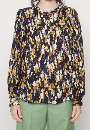 Blusa multicolor con base azul marino oscuro, con un audaz patrón abstracto en amarillo, blanco y marrón, frente abotonado y mangas abullonadas.