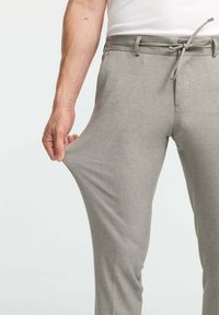 Light gray pants made of a textured fabric, featuring a drawstring waist and side pockets, displayed with a hand pulling at the fabric.