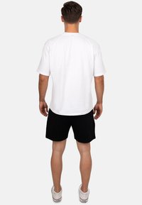 Witte t-shirt met korte mouwen en ronde hals, ontspannen pasvorm, gedragen met zwarte shorts en witte sneakers; gladde textuur zichtbaar.