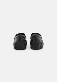 Scarpe in pelle nera con forma arrotondata, dotate di una suola in gomma rigata e un design liscio e minimalista. Nessun motivo o accento visibile.