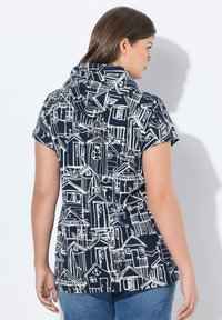 Camiseta corta con capucha que presenta un fondo azul marino con patrones de casas dibujadas en blanco. Mezcla de algodón, corte relajado, diseño casual.