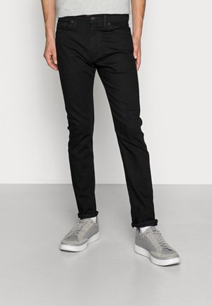 Jeans de ganga pretos com um corte slim, apresentando um design de cinco bolsos, costuras subtis e uma cintura média, combinados com ténis cinza claro.
