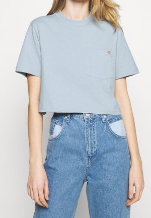 Kort, lyseblå bomuldst-shirt med rund hals og venstre brystlomme. Kombineret med højttaljede, lyseblå denimjeans.