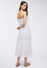Abito maxi bianco a strati con spalline regolabili e design fluido. Tessuto leggero e vestibilità ampia offrono comfort. Ottimo per il clima caldo.