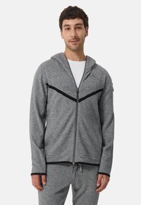 Grå fleece zip-up hoodie med svarta accentremsor, som har en huva, en framdragkedja och ribbade ärmslut. En enfärgad vit t-shirt under.