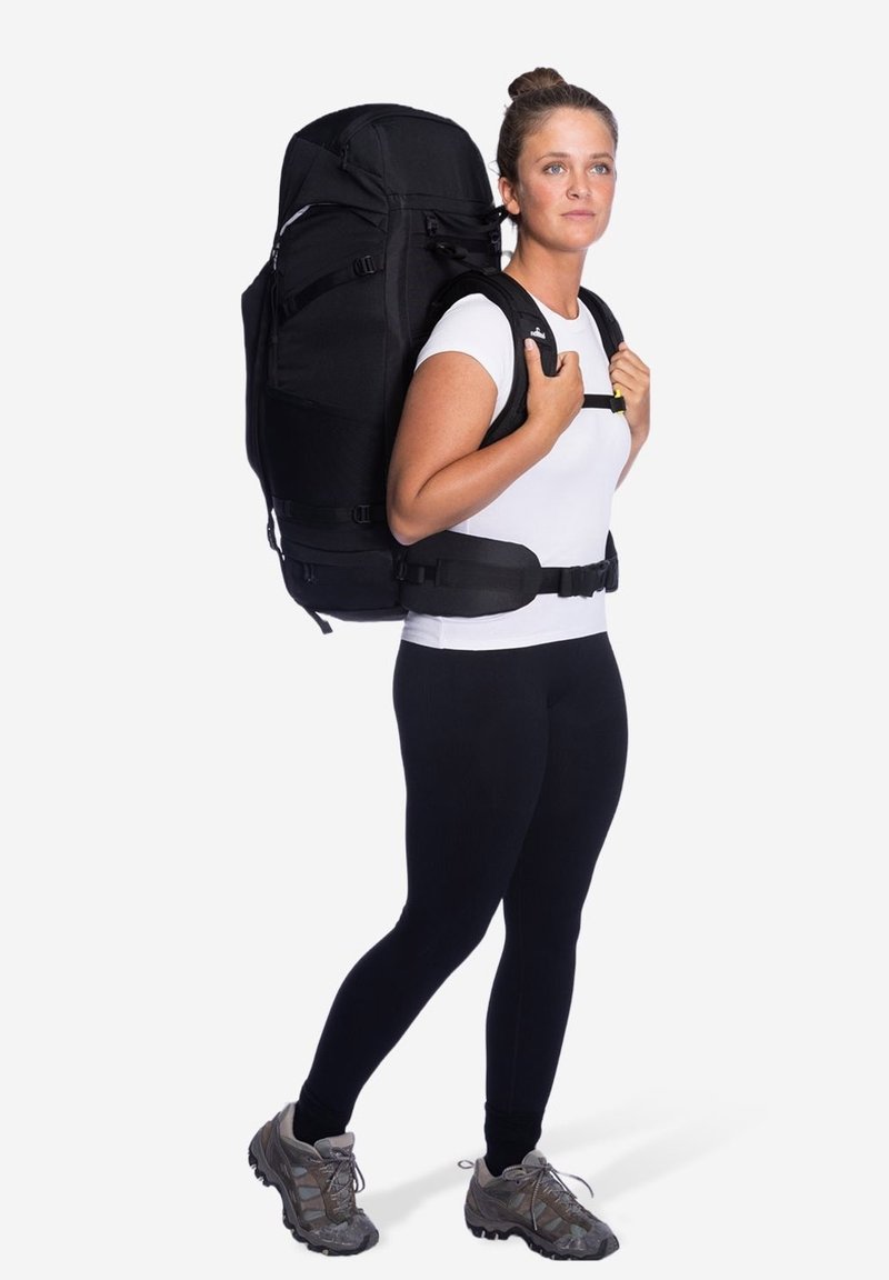 Zwarte wandelrugzak met meerdere compartimenten, verstelbare schouderbanden en een gevoerde heupriem, gedragen door een persoon in een aansluitend wit shirt en zwarte leggings.