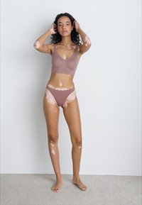 Bruine geribbelde bralette en bijpassende bikinionderkant. Glad textuur, minimalistisch ontwerp, geschulpte randen, gedragen tegen een effen achtergrond.