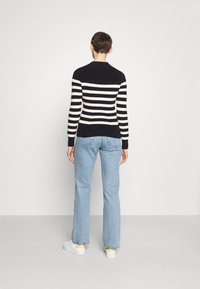 Marineblau- und crèmefarbener gestreifter Strickpullover mit rundem Ausschnitt und langen Ärmeln, kombiniert mit hellblauen geraden Jeans und weißen Sneakers.