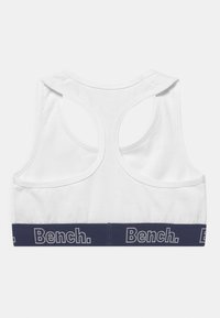 Hvit sports-BH med racerback-design, med et marineblått elastisk bånd med "Bench."-logo. Laget av mykt bomullsmateriale.