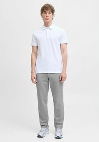 Biała koszulka polo z kołnierzykiem i trzema guzikami, w połączeniu z szarymi dresami. Buty w jasnoszarym kolorze z niebieskimi akcentami. Całość ma prosty design.