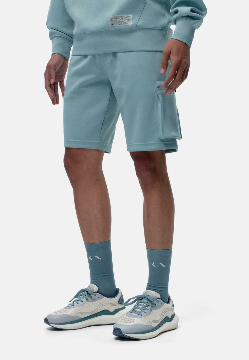 Sudadera de color azul claro con una etiqueta, combinada con pantalones cortos a juego de color azul claro que cuentan con un bolsillo lateral. Usada con zapatillas deportivas y calcetines de color azul claro.