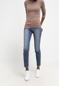 Grå långärmad topp med rund halsringning, kombinerad med ljusblå tajta jeans och vita platta sneakers.