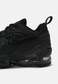 Černá sportovní obuv s texturovaným syntetickým svrškem, elegantním designem, viditelným vzduchovým polstrováním a poutkem na patě pro snadné nazouvání.