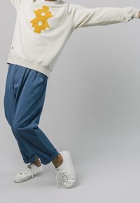 Lichtcrème sweatshirt met een gele geometrische print, gecombineerd met een paarse textuur blauwe broeken en witte sneakers, en toont een ontspannen pasvorm en casual stijl.