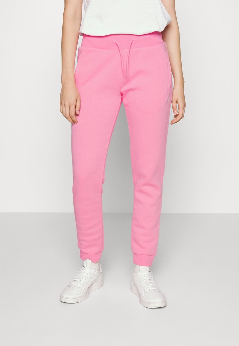 Pantalones de chándal rosa con cintura ajustable, puños entallados y bolsillos laterales, hechos de una tela suave y texturizada. Combinados con zapatillas blancas.