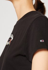 Černé bavlněné tričko s barevným květinovým vyšíváním a malým logem na rukávu. Krátké rukávy a kulatý výstřih.