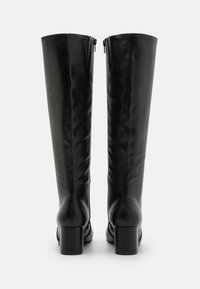 Bottes montantes noires en cuir avec une texture lisse, talons carrés et fermetures éclair latérales pour un enfilage facile. Design minimaliste sans motifs visibles.