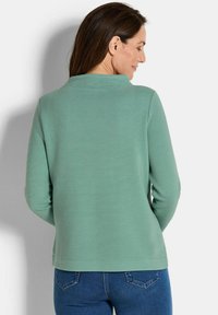 Groen geribbelde lange mouwen top met een ronde halslijn, textuurstof en een rechte zoom, gecombineerd met donkerblauwe jeans.