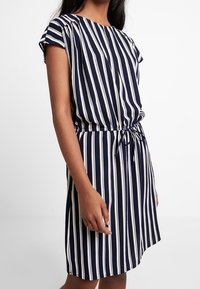 Vestido a rayas en azul marino y blanco con mangas cortas, cintura ceñida y lazo ajustable, que cuenta con un escote redondo y una textura suave.