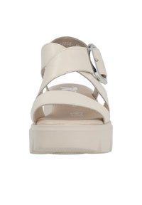 Sandale en cuir beige avec une semelle épaisse, deux brides croisées sur le pied, et une boucle argentée sur le côté extérieur.
