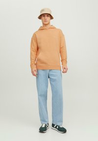 Oranžs kokvilnas hoodie ar kenguru kabatu, savienots ar gaiši ziliem denim džinsiem. Izskatu papildina bēša bucket cepure. Melni sporta apavi ar baltām akcentiem.