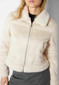 Giacca in finta suede color crema con colletto e polsini in shearling, design aderente, chiusura con zip e dettagli cuciti sulle spalle e in vita.
