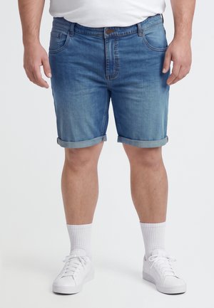 Modèle portant un short en jean bleu à revers, un T-shirt blanc, des chaussettes blanches et des baskets blanches.