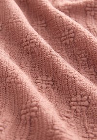 Tissu tricoté rose poudré doux avec des motifs en forme de losange en relief et un tissage texturé, présenté en plis doux.