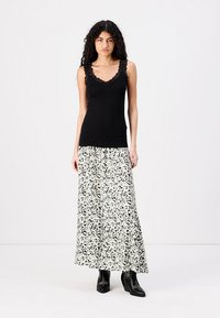 Black tank top with lace trim paired with a white and black patterned maxi skirt. Model wears black ankle boots. Flat background.