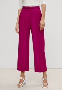 Fuksjowe spodnie o szerokich nogawkach z wysokim stanem, plisami z przodu i dwoma guzikami. Materiał wydaje się gładki i lekki.