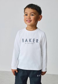 Weißes Langarmhemd mit der Aufschrift "BAKER by TED BAKER" in dunkler Schrift. Getragen zu dunklen Cargohosen, vor neutralem Hintergrund präsentiert.