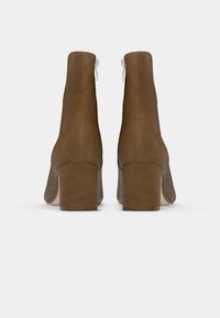 Paire de bottines en daim marron à talons blocs vues de dos sur fond blanc uni.