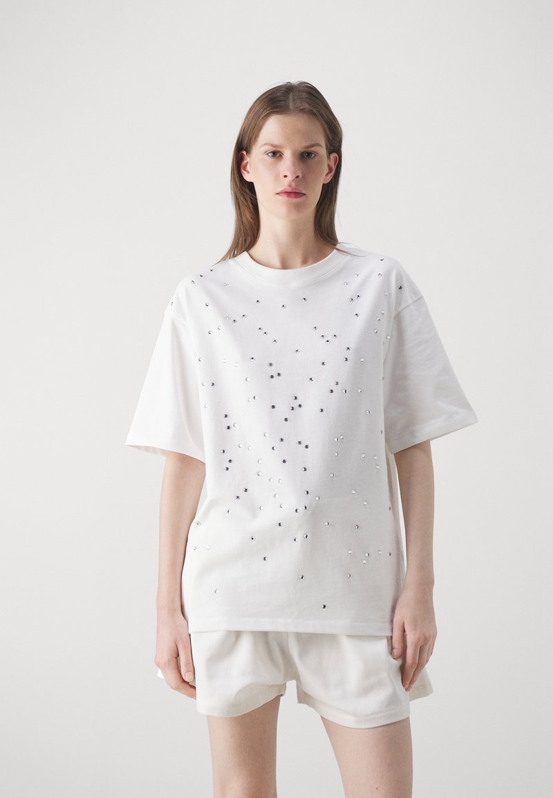 White cotton t-shirt with a relaxed fit, featuring scattered silver and black embellishments across the front and short sleeves.