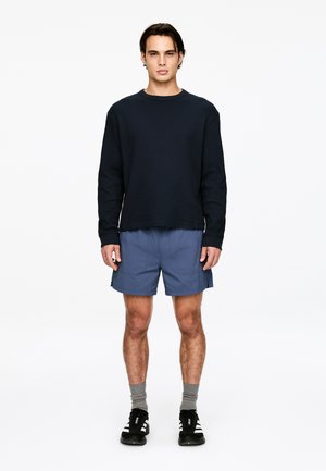 Navy textured long-sleeve shirt paired with light blue shorts. Model wears gray socks and black sneakers with white accents.