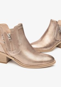 Bottines métalliques en or rose, en cuir perforé, avec un bout pointu, des panneaux élastiques sur les côtés et une fermeture éclair latérale, dotées d'un talon en bois empilé.