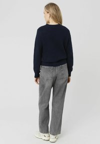 Pull court bleu marine avec ourlet côtelé et manches longues, associé à un jean gris à taille haute et à coupe ample. Chaussures dans des tons neutres.