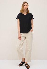 Sort kortærmet top med bundet ærmer, parret med lyse beige vide bukser og sorte sandaler med en guldspænde.