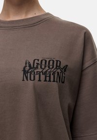 Bruine katoenen sweatshirt met een zwarte grafische print waarin "PRESENTED BY GOOD FOR NOTHING" staat, vergezeld van vlinderillustraties.