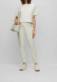 Osoba w białej, krótkiej koszulce, w beżowych spodniach o wysokim stanie, w beżowo-białych trampkach, trzymająca białą torebkę na ramię.