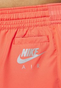 Shorts de Nike en un vibrante tejido coral, con cintura elástica, un bolsillo trasero y un logo plateado de "Nike Air" en la parte delantera.