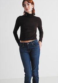 Čierny cropovaný rolák s dlhými rukávmi kombinovaný s tmavomodrými priliehavými džínsami. Hladká tkanina, jednoduchý dizajn, minimálne detaily.