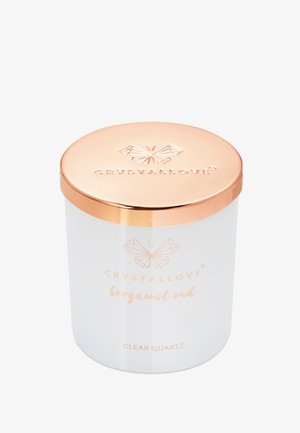 Biały szklany świecznik z różowozłotą metalową pokrywką. Posiada wytłoczone logo oraz nazwę produktu "Bergamot Oud." Przezroczysty kwarc wskazany na dole.