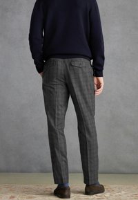 Pantalons à carreaux gris avec une coupe ajustée, deux poches arrière avec boutons, et une texture lisse. Portés avec un pull bleu marine et des chaussures marron.