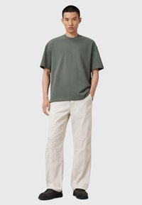 Mørkegrøn kortærmet t-shirt, afslappet pasform, parret med crème cargo bukser med kontrastsyninger og mørke slip-on sko.