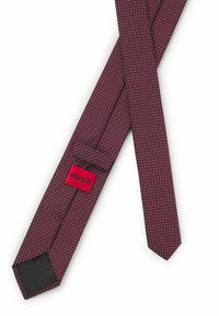 Burgundy tie with white polka dots, made of textured fabric. Features a black interior and a red label with "HUGO" and "MADE IN ITALY."